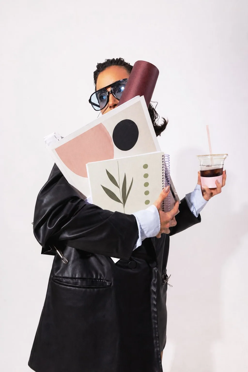 Woman in a leather coat carrying editorial notebooks and coffee