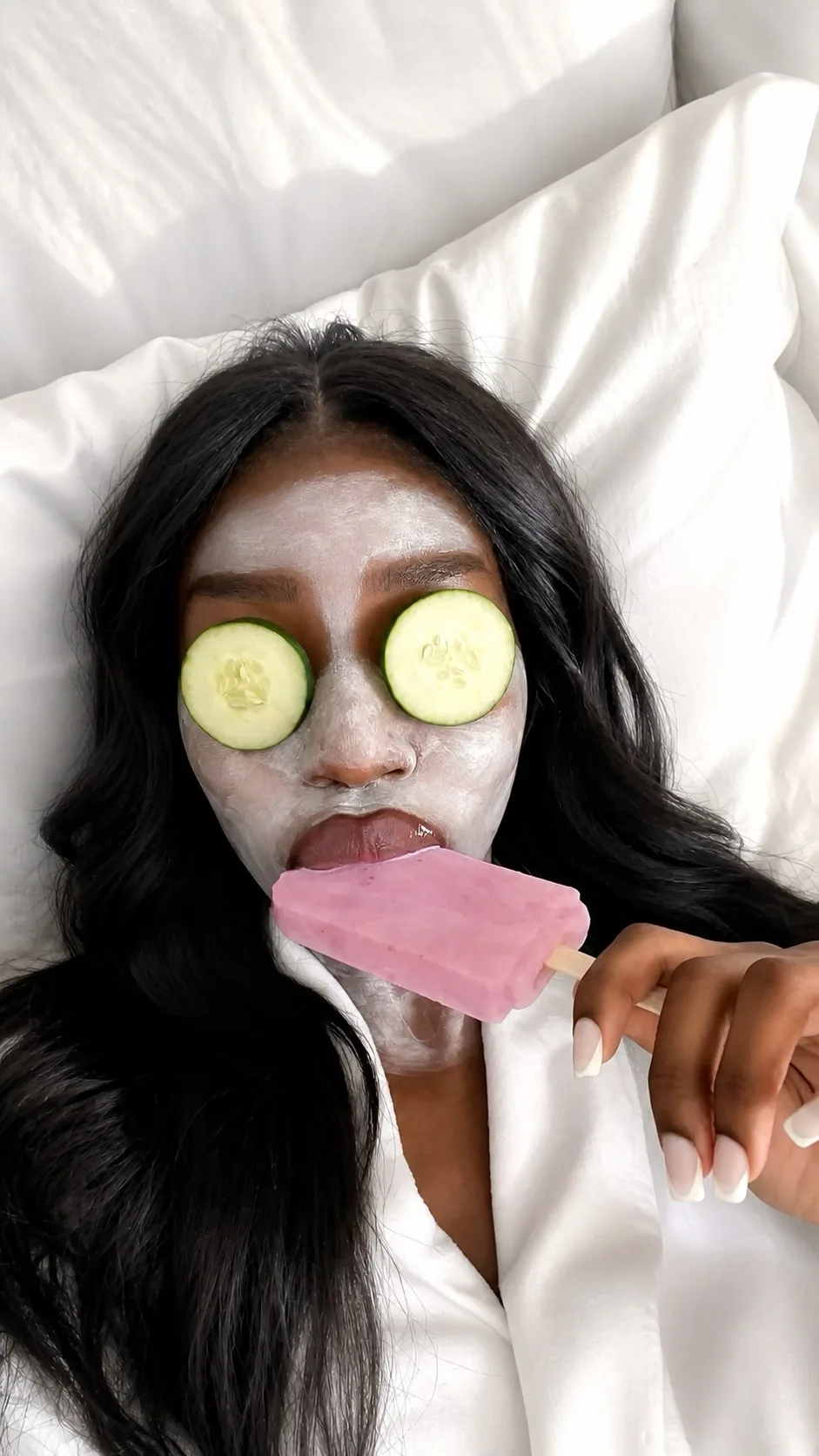 Woman relaxing with a face mask, cucumber slices, and a pink ice pop