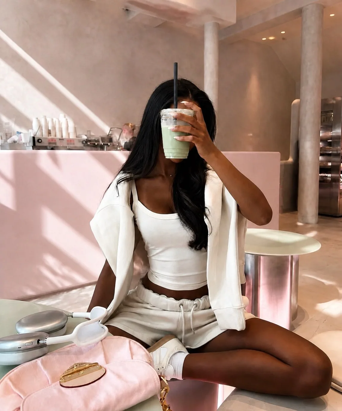Woman in white activewear enjoying a green drink in a blush cafe